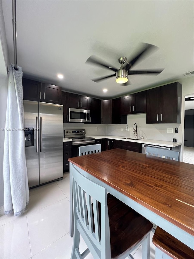 kitchen with stainless steel appliances, light tile patterned floors, ceiling fan, dark brown cabinetry, and sink