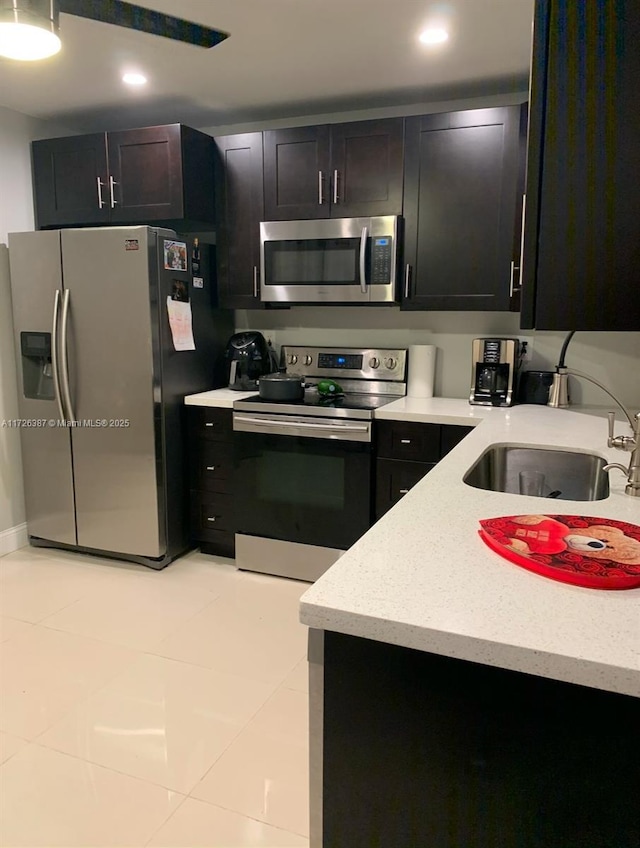 kitchen featuring stainless steel appliances, a sink, recessed lighting, light tile patterned flooring, and dark cabinets