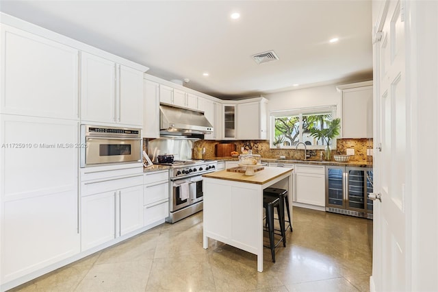 kitchen with a center island, butcher block countertops, stainless steel appliances, white cabinets, and beverage cooler