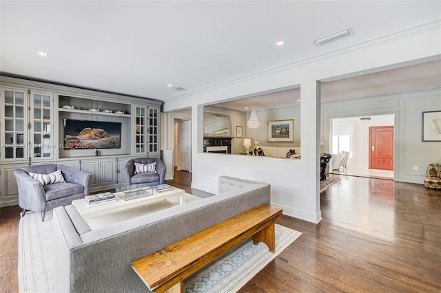 living room featuring built in shelves, dark hardwood / wood-style flooring, and ornamental molding