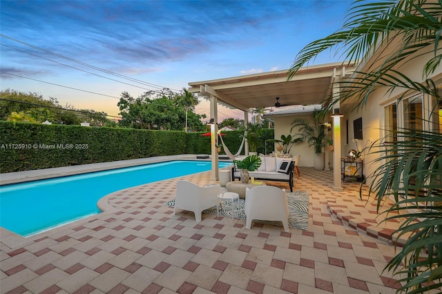 pool at dusk with ceiling fan, outdoor lounge area, and a patio