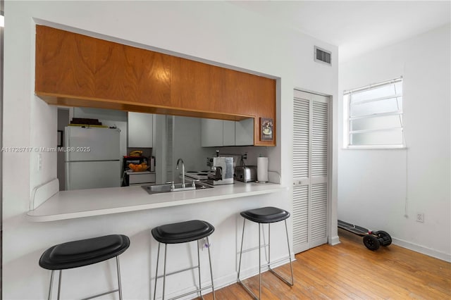 kitchen featuring light wood-type flooring, kitchen peninsula, a breakfast bar, white refrigerator, and sink