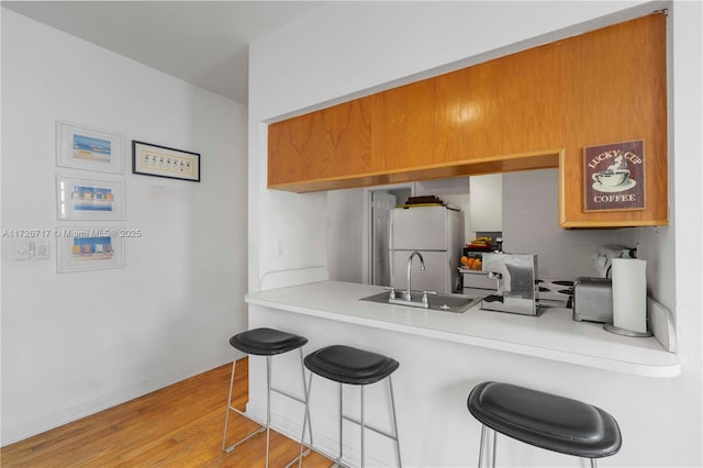 kitchen featuring a kitchen breakfast bar, hardwood / wood-style floors, kitchen peninsula, white refrigerator, and sink