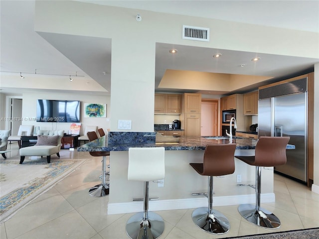 kitchen featuring kitchen peninsula, built in appliances, a tray ceiling, sink, and a kitchen bar