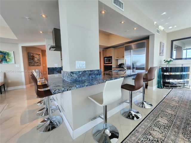 kitchen with built in appliances, light tile patterned floors, a breakfast bar area, and kitchen peninsula