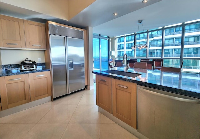 kitchen featuring appliances with stainless steel finishes, light tile patterned flooring, hanging light fixtures, and dark stone countertops