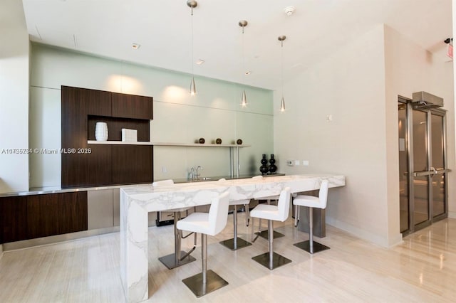 interior space with dark brown cabinets, hanging light fixtures, a breakfast bar area, sink, and kitchen peninsula