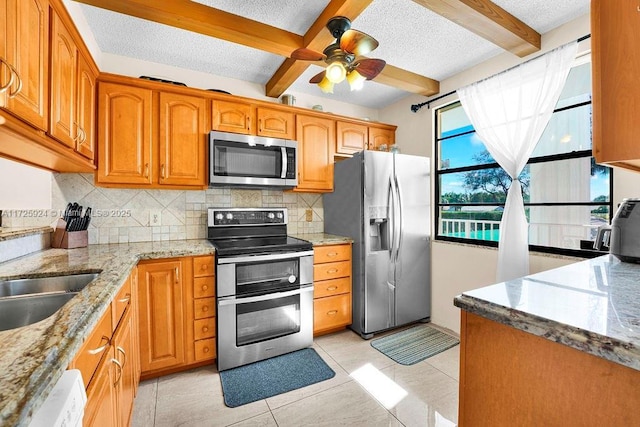 kitchen featuring light tile patterned floors, appliances with stainless steel finishes, tasteful backsplash, light stone countertops, and beamed ceiling