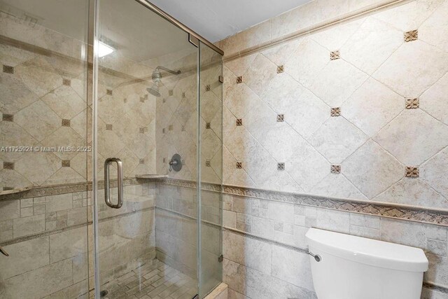 bathroom with toilet, tile walls, and a shower with shower door