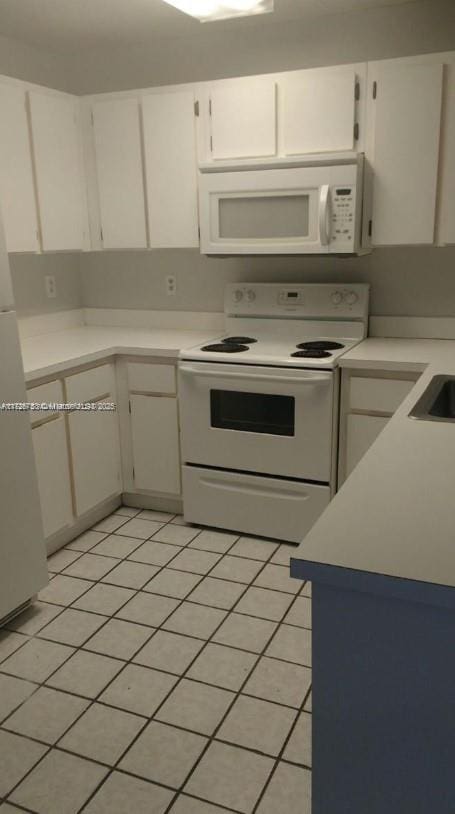 kitchen with white cabinets, light tile patterned floors, and white appliances