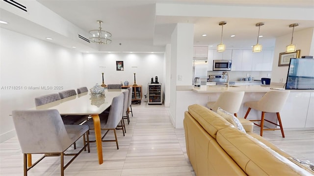 kitchen with hanging light fixtures, stainless steel appliances, an inviting chandelier, white cabinets, and sink