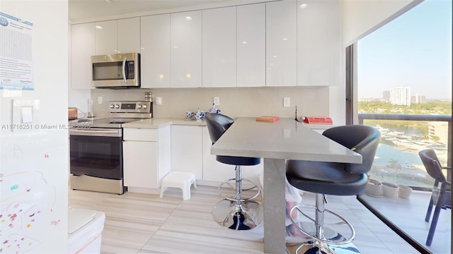 kitchen with stainless steel appliances, light tile patterned flooring, white cabinetry, and a breakfast bar