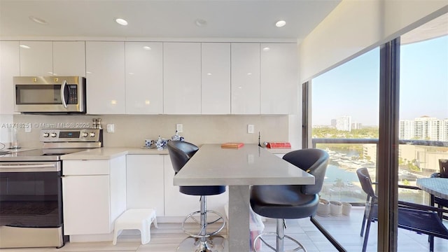 kitchen featuring a kitchen breakfast bar, decorative backsplash, white cabinetry, and appliances with stainless steel finishes