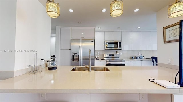 kitchen featuring kitchen peninsula, decorative light fixtures, white cabinetry, appliances with stainless steel finishes, and sink