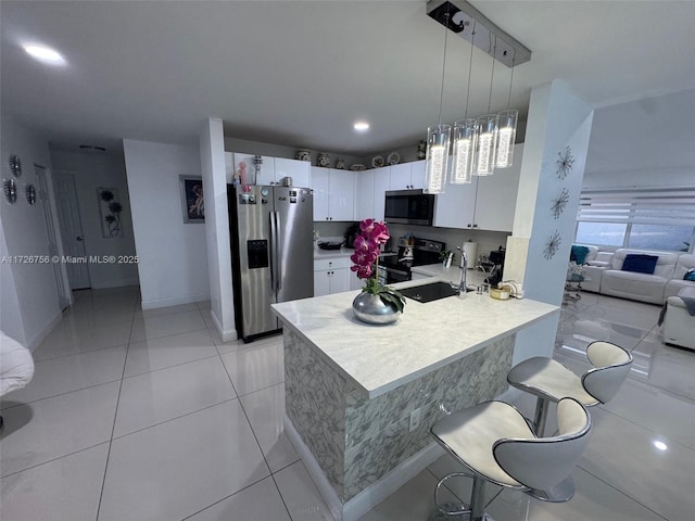 kitchen with light tile patterned flooring, appliances with stainless steel finishes, white cabinets, a kitchen breakfast bar, and hanging light fixtures