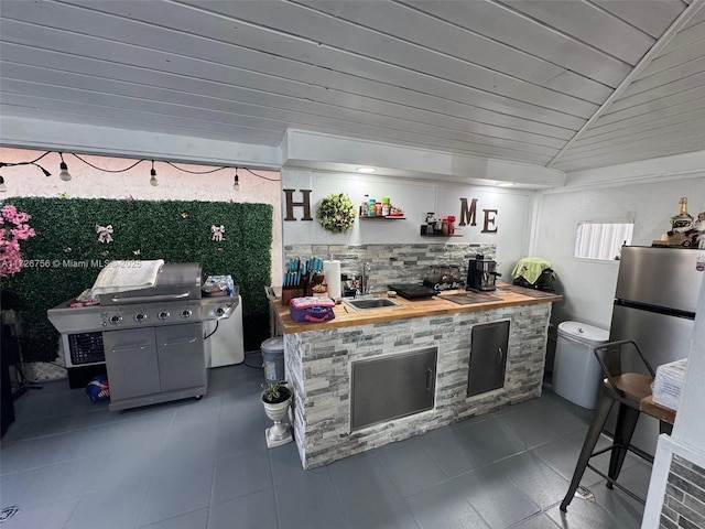 kitchen featuring vaulted ceiling, sink, stainless steel fridge, and butcher block countertops