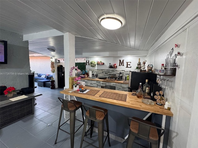 bar with wooden counters, tile patterned flooring, decorative backsplash, vaulted ceiling, and wooden ceiling