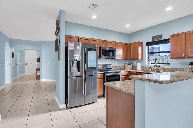 kitchen with kitchen peninsula, appliances with stainless steel finishes, light tile patterned flooring, light stone countertops, and sink