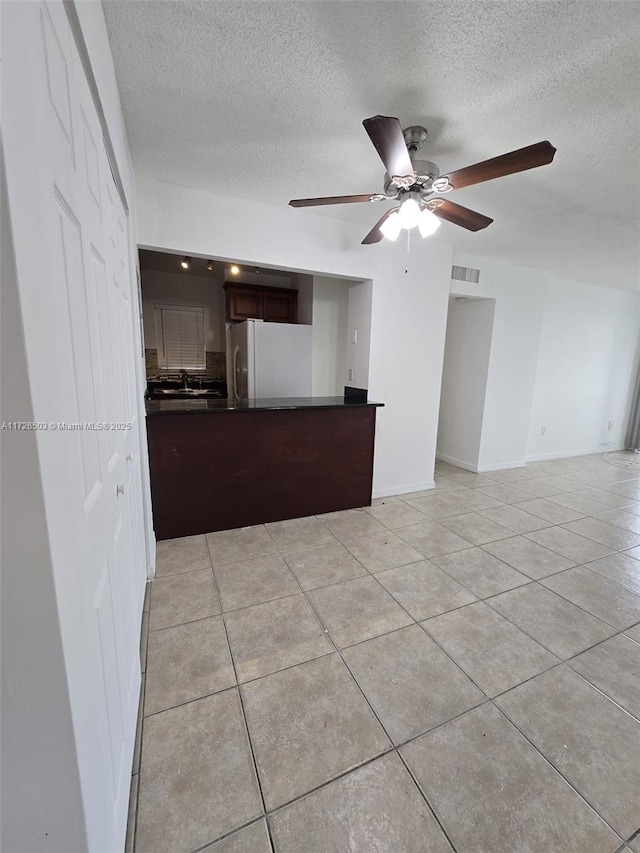 kitchen with a textured ceiling, dark brown cabinetry, white fridge, light tile patterned flooring, and ceiling fan