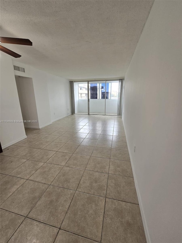 tiled empty room with ceiling fan and a textured ceiling