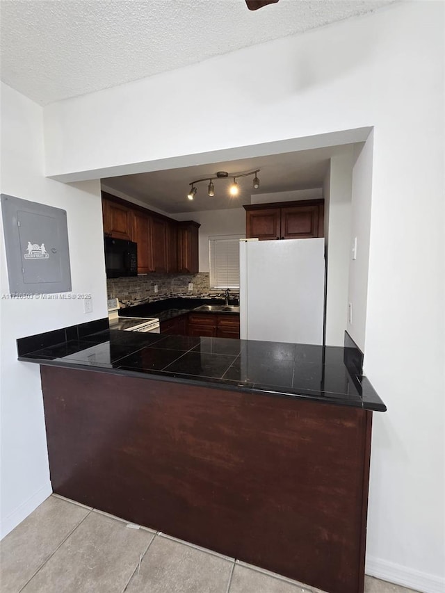 kitchen with white fridge, kitchen peninsula, sink, a textured ceiling, and light tile patterned floors