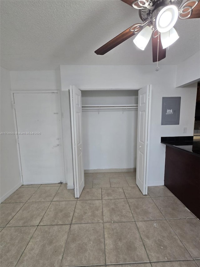 unfurnished bedroom with a textured ceiling, ceiling fan, electric panel, and light tile patterned floors