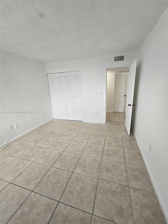 unfurnished bedroom with a textured ceiling, a closet, and light tile patterned floors