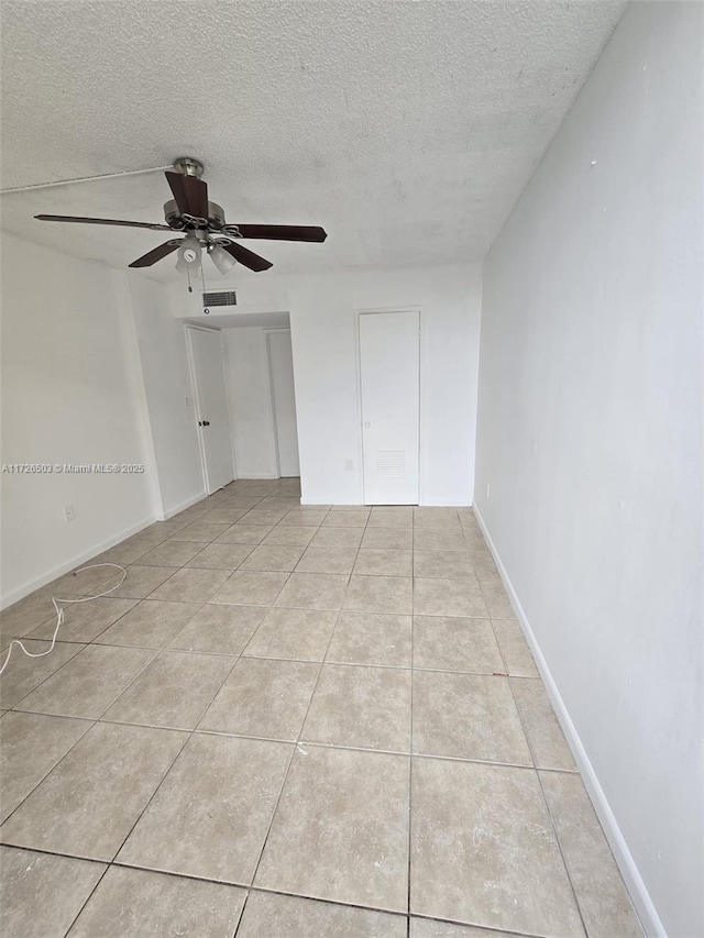 empty room with ceiling fan, light tile patterned floors, and a textured ceiling