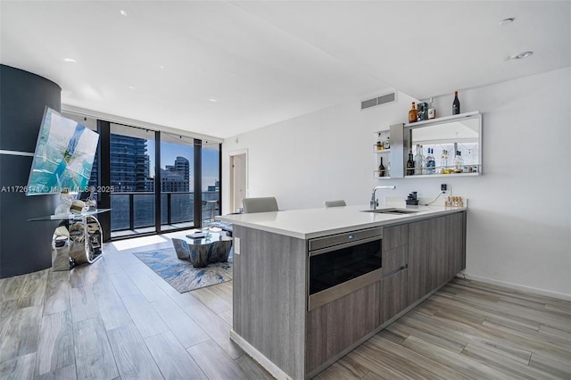 kitchen featuring floor to ceiling windows, kitchen peninsula, light hardwood / wood-style flooring, and sink