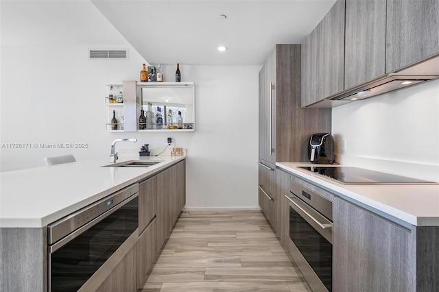 kitchen with a sink, modern cabinets, black electric stovetop, light countertops, and stainless steel oven