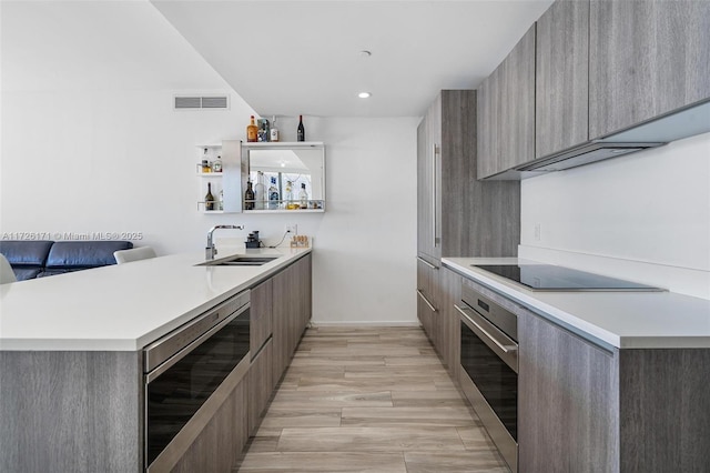 bar with a sink, black electric cooktop, oven, visible vents, and beverage cooler