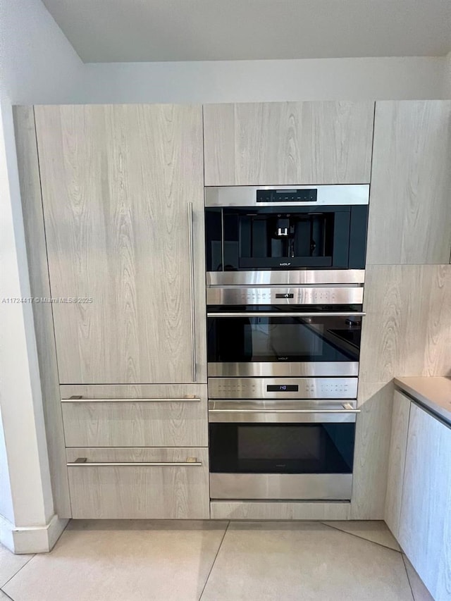 kitchen featuring light brown cabinets, light tile patterned flooring, and stainless steel double oven