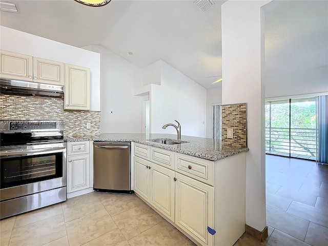 kitchen featuring light stone counters, vaulted ceiling, decorative backsplash, appliances with stainless steel finishes, and sink