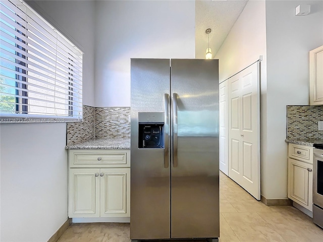 kitchen with cream cabinetry, stainless steel appliances, hanging light fixtures, light stone countertops, and backsplash