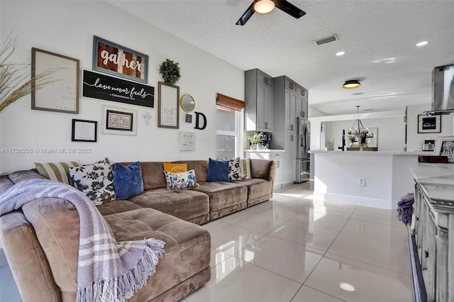 tiled living room with a textured ceiling and ceiling fan with notable chandelier