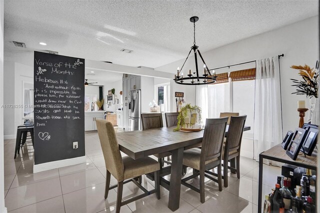 tiled dining space with ceiling fan with notable chandelier and a textured ceiling