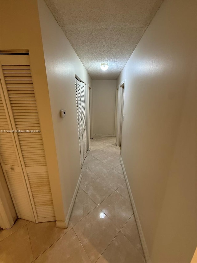 hallway with a textured ceiling and light tile patterned floors