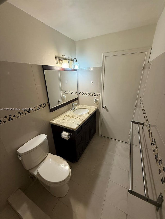 bathroom with toilet, tile patterned flooring, vanity, and tile walls