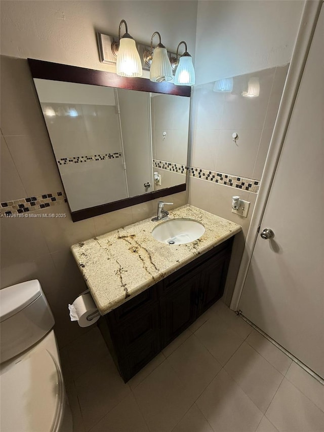 bathroom with toilet, tile patterned flooring, vanity, and tile walls