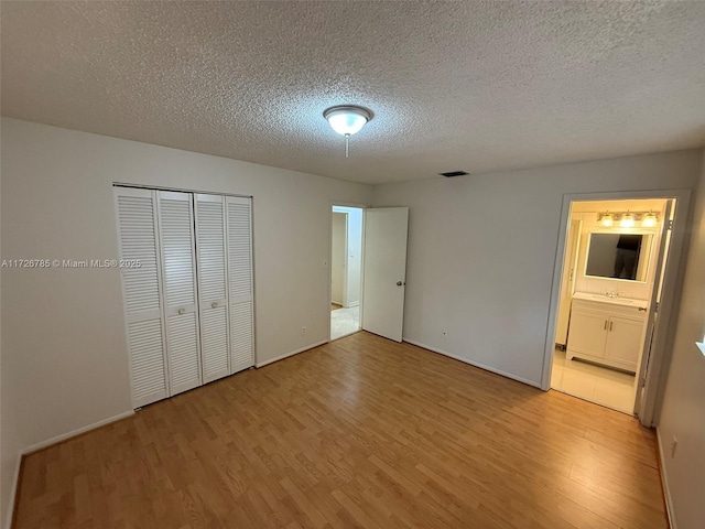 unfurnished bedroom featuring a textured ceiling, a closet, light hardwood / wood-style flooring, and connected bathroom