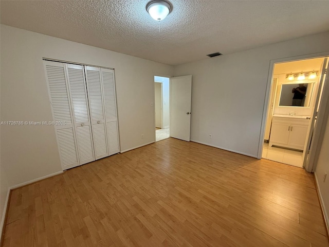 unfurnished bedroom featuring ensuite bath, light wood-type flooring, a closet, and a textured ceiling