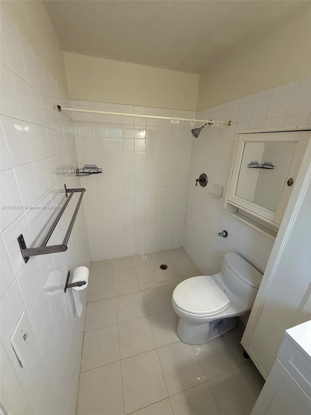 bathroom with toilet, a tile shower, tile patterned flooring, and tile walls