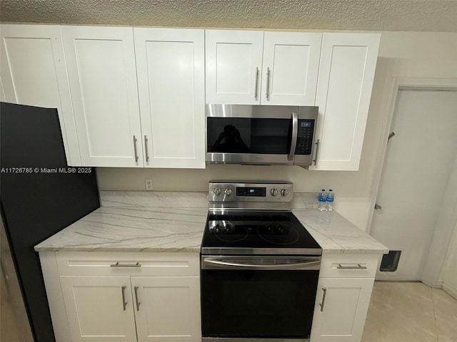 kitchen with appliances with stainless steel finishes, white cabinetry, light stone counters, and light tile patterned floors