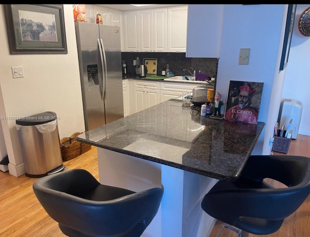 kitchen featuring tasteful backsplash, white cabinets, dark stone counters, stainless steel fridge with ice dispenser, and light hardwood / wood-style flooring