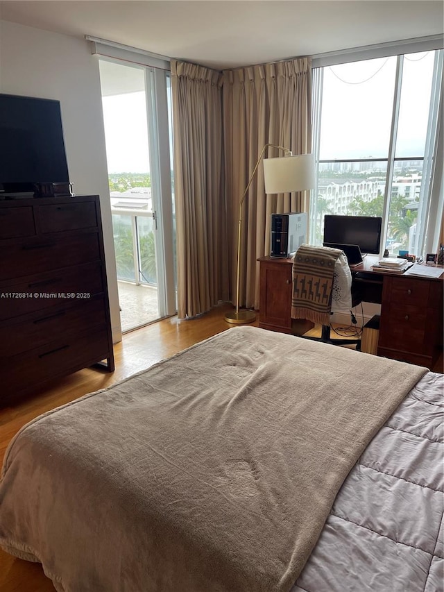 bedroom featuring a wall of windows, light hardwood / wood-style flooring, multiple windows, and access to outside