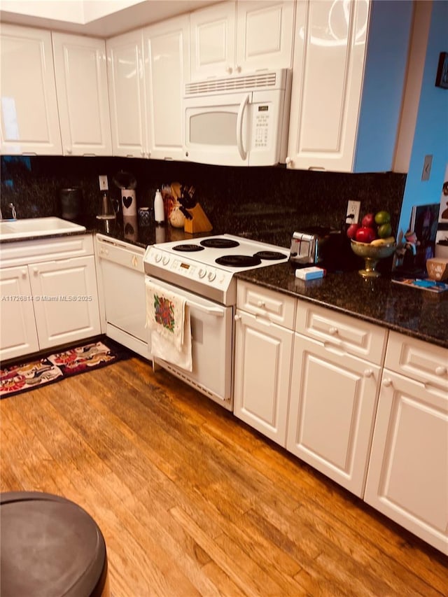 kitchen with sink, white appliances, white cabinetry, dark stone counters, and light wood-type flooring