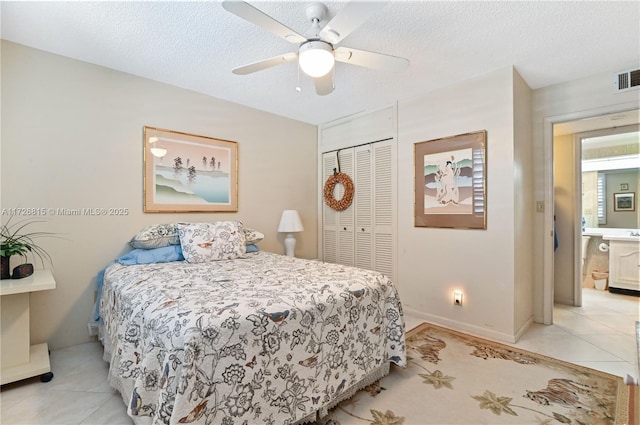 tiled bedroom with ceiling fan, connected bathroom, a closet, and a textured ceiling