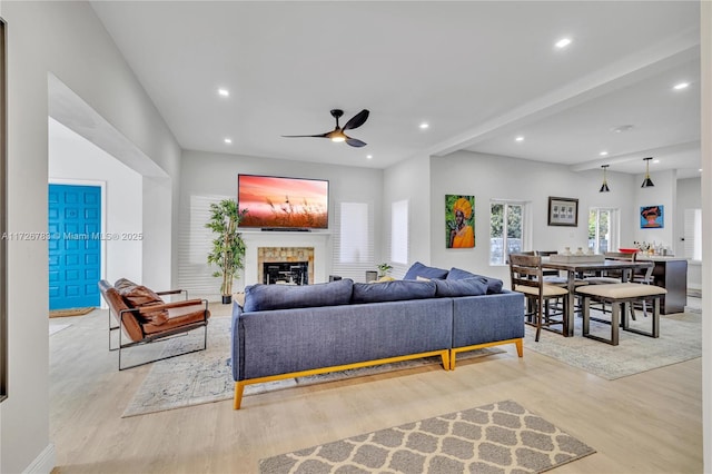 living room with a fireplace, ceiling fan, light hardwood / wood-style floors, and beam ceiling