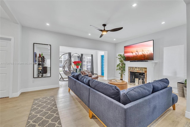 living room featuring ceiling fan, light wood-type flooring, and a fireplace