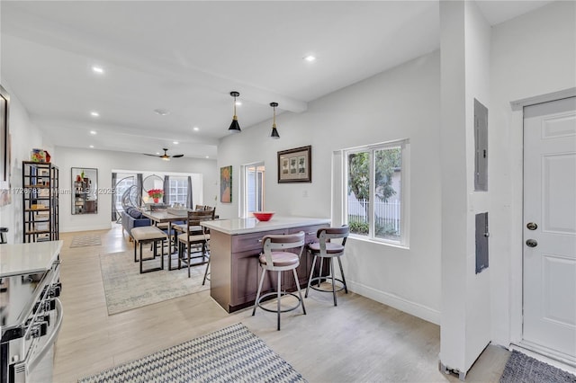 kitchen featuring kitchen peninsula, stainless steel range oven, decorative light fixtures, light hardwood / wood-style floors, and a breakfast bar